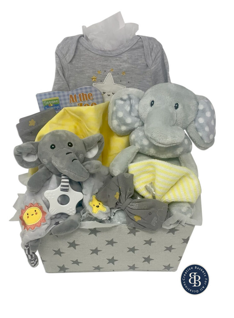 Baby gift basket with two plush grey elephants, a star onesie, yellow blankets, a teether and a board book in a star print box